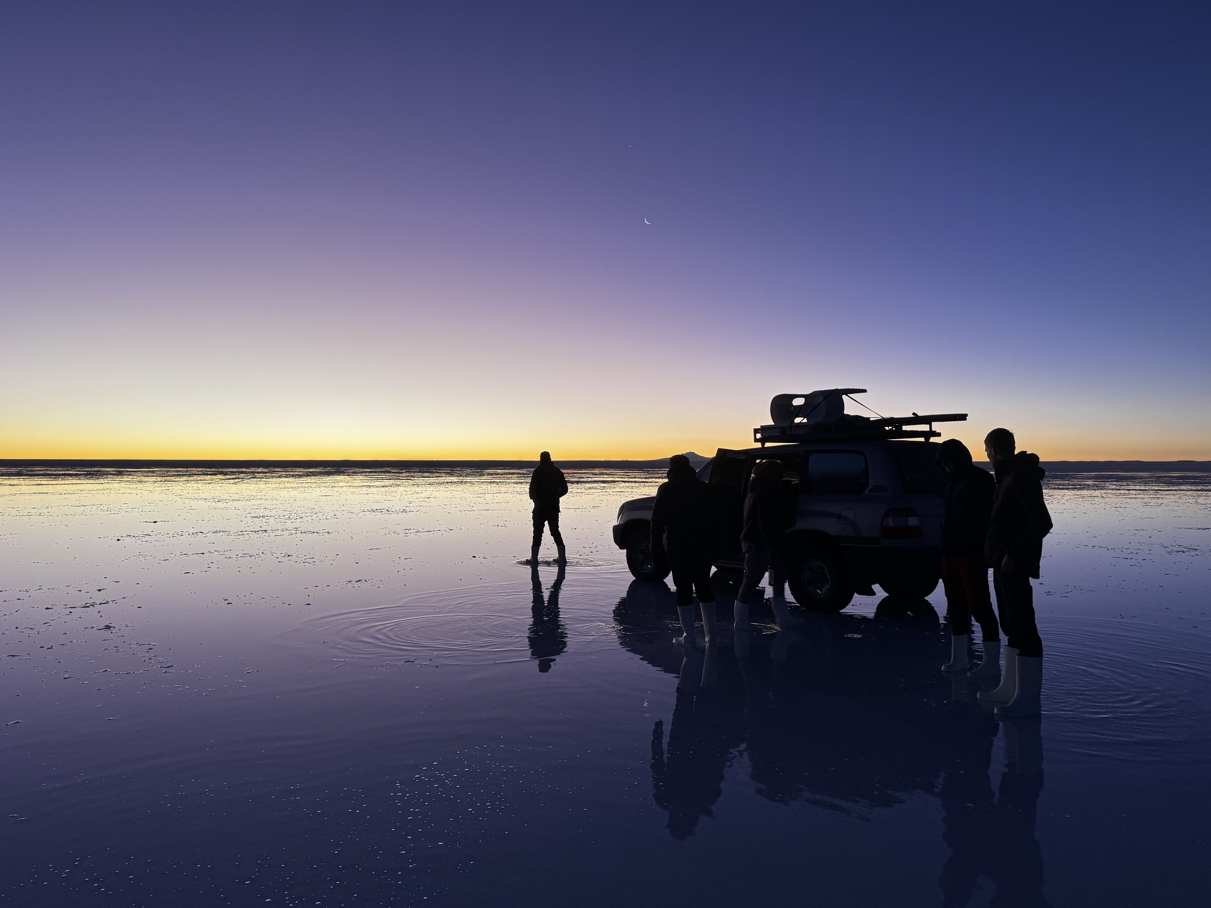 Travelers and a four-wheel-drive vehicle at sunrise on the Uyuni salt flats